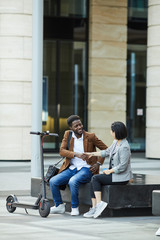 Wall Mural - Portrait of smiling African-American man shaking hands with Asian woman while sitting on bench outdoors, copy space