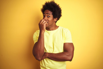 Poster - African american man with afro hair wearing t-shirt standing over isolated yellow background looking stressed and nervous with hands on mouth biting nails. Anxiety problem.