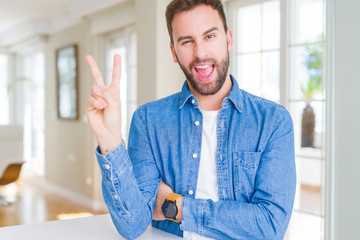 Wall Mural - Handsome man at home smiling with happy face winking at the camera doing victory sign. Number two.