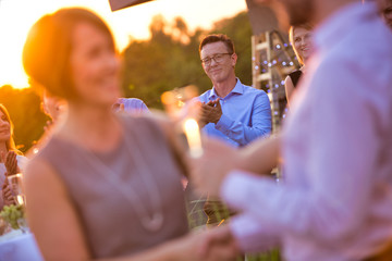 Wall Mural - Young businessman shaking hands with mature businesswoman during rooftop party