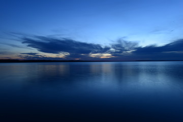 Wall Mural - blue sky in the twilight glow from behind clouds over the azure calm surface of the water