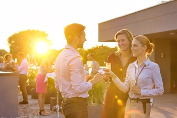 Young businesswoman giving business card to colleague while holding wine glass on success party at rooftop