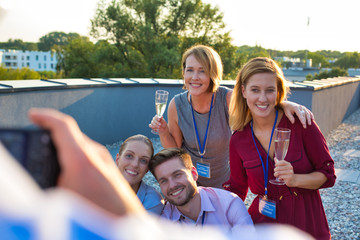 Canvas Print - Businessman photographing colleagues during rooftop success party