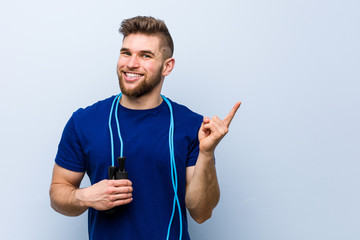 Wall Mural - Young caucasian sportsman with a jump rope smiling cheerfully pointing with forefinger away.