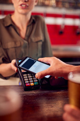 close up of man paying for drinks at bar using contactless app on mobile phone