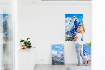 Wall Mural - Young woman hangs the art picture on wall at home