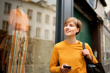 young woman walking in city with mobile phone and bag