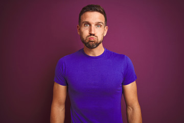 Poster - Young man wearing casual purple t-shirt over lilac isolated background puffing cheeks with funny face. Mouth inflated with air, crazy expression.