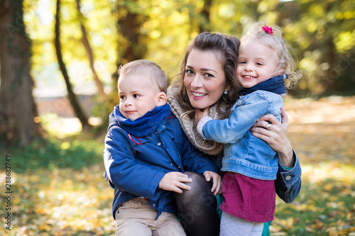 Fotomural Beautiful young mother with small twins on a walk in autumn forest