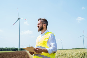 Wall Mural - An engineer standing on a field on wind farm, making notes.