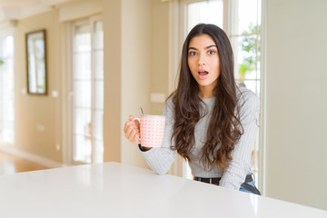 Poster - Young woman drinking a cup of coffee scared in shock with a surprise face, afraid and excited with fear expression