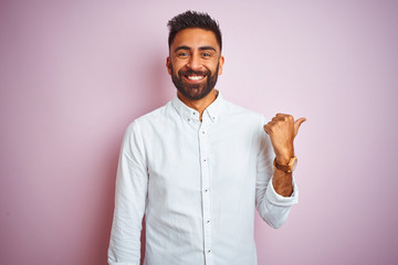 Young indian businessman wearing elegant shirt standing over isolated pink background smiling with happy face looking and pointing to the side with thumb up.