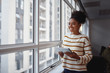 © StratfordProductions - Smiling thoughtful beautiful young african american businesswoman with digital tablet standing at the office window looking away
