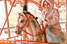 A Little Girl In Bright Clothes Is Riding On A Merry-go-round With Horses. Happy Child.
