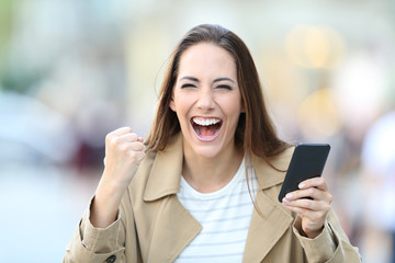 Wall Mural - Excited woman holding phone looking at camera