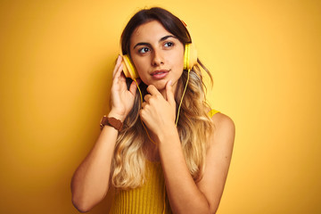 Canvas Print - Young beautiful woman wearing headphones over yellow isolated background serious face thinking about question, very confused idea