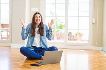 Poster - Beautiful young woman sitting on the floor with crossed legs using laptop celebrating mad and crazy for success with arms raised and closed eyes screaming excited. Winner concept