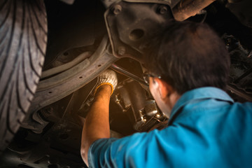 Wall Mural - mechanic repairing a car, mechanic inspects car suspension system and chassis with a torch-lite unde