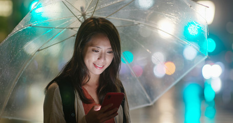 Canvas Print - Woman hold with umbrella and look at the cellphone at night