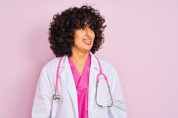 Sticker - Young arab doctor woman with curly hair wearing stethoscope over isolated pink background looking away to side with smile on face, natural expression. Laughing confident.