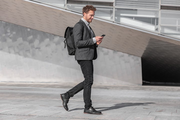 Wall Mural - happy young business man using phone walking on commute commuting to work with backpack bag on city 