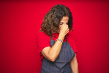 Middle Age Senior Woman Wearing Apron Uniform Over Red Isolated Background Tired Rubbing Nose And Eyes Feeling Fatigue And Headache. Stress And Frustration Concept.