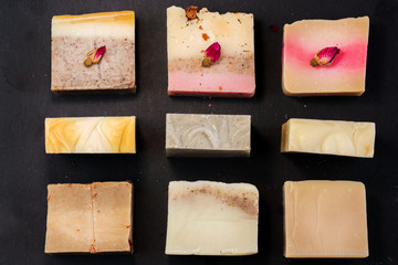 Fototapete - handmade multicolored soap with herbs and rosebuds on a black background with a blank space for text. Spa soap for face and body treatments flat lay istagram  style