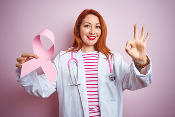 Sticker - Young redhead doctor woman holding cancer ribbon over pink isolated background doing ok sign with fingers, excellent symbol