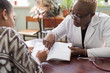 © Алексей Доненко - Hispanic patient signs treatment agreement with African female doctor. Young people of mixed race. The trust of the patient and the doctor. Voluntary Informed Consent