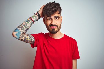 Sticker - Young man with tattoo wearing red t-shirt standing over isolated white background confuse and wonder about question. Uncertain with doubt, thinking with hand on head. Pensive concept.