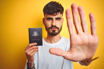 Poster - Young man with tattoo wearing Australia Australian passport over isolated yellow background with open hand doing stop sign with serious and confident expression, defense gesture