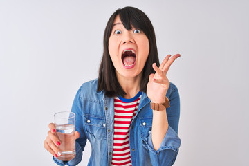 Wall Mural - Young beautiful Chinese woman holding glass of water over isolated white background very happy and excited, winner expression celebrating victory screaming with big smile and raised hands