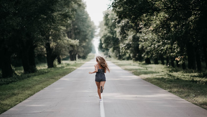 long-haired girl rear view runs along a forest road runs away from fears to meet a brighter future