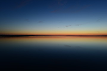 Wall Mural - Nightfall blue hour twilight glow on the horizon in calm on the water and in the sky
