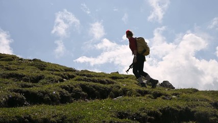 Wall Mural - Girl photographer goes uphill on the background and the sky with clouds on a sunny day. Concept photo tours for landscape photographers. Mountain trekking