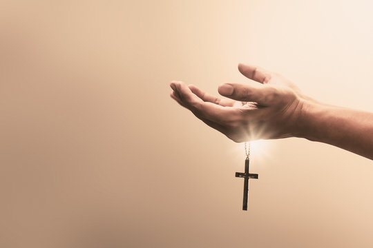 Praying hands hold a crucifix or cross of metal necklace with faith in religion and belief in God on confession background. Power of hope or love and devotion.