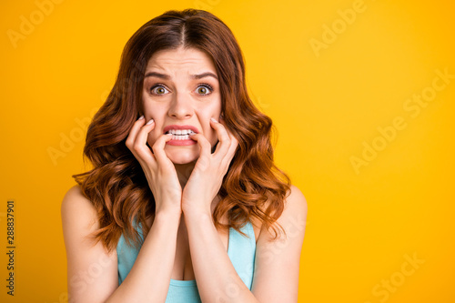Photo of terrible feared girlfriend driven mad with some sorrow happened to her biting nails with panic while wearing teal tank-top isolated with yellow vivid color background
