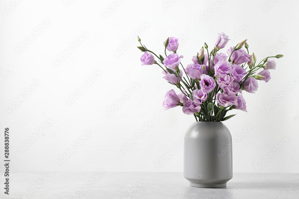 Eustoma flowers in vase on table near white wall, space for text - obrazy, fototapety, plakaty 