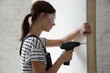 © triocean - Young woman drilling screws into plasterboard with an electric screwdriver, home improvement concept