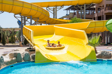 On a bright sunny day at the water park, the family slides down the hill on an air mattress.