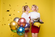© Вячеслав Косько - Two happy beautiful woman friend celebrating posing surrounded by colorful air balloon confetti. Attractive smiling female wearing bright clothes enjoying party isolated at yellow studio background