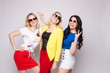 © Вячеслав Косько - Three cheerful women wearing bright colorful skirts, shirts and glasses standing on grey isolated background. Happy girls looking at camera, laughing and showing tongue. Concept of happiness.