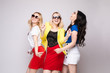© Вячеслав Косько - Three cheerful women wearing bright colorful skirts, shirts and glasses standing on grey isolated background. Happy girls looking at camera, laughing and showing tongue. Concept of happiness.