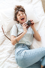 Sticker - Happy cheery positive woman indoors at home lies on bed in the morning holding camera photographing.