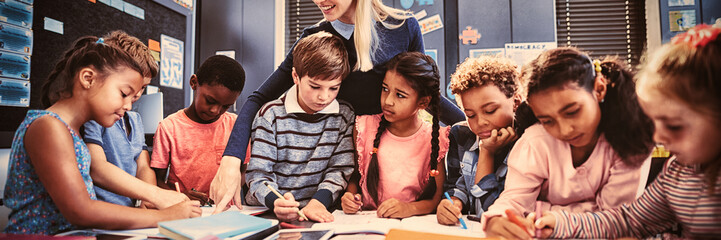 Teacher helping schoolgirl with her homework in classroom