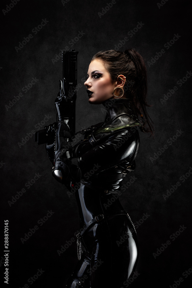 Portrait of a young woman in latex overalls holding a futuristic weapon in her hands - obrazy, fototapety, plakaty 