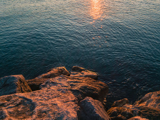 Wall Mural - Large stones on the seashore in the orange light of the setting sun glinting on the turquoise water surface of the sea on a summer evening.