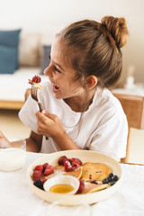 Wall Mural - portrait of cute little girl smiling while having breakfast and eating pancakes at home