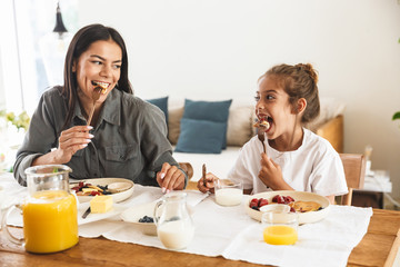 Wall Mural - image of beautiful family mother and little daughter eating together while having breakfast at home 