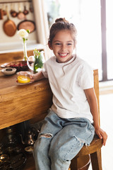 Portrait of young little girl having breakfast and drinking orange juice at home